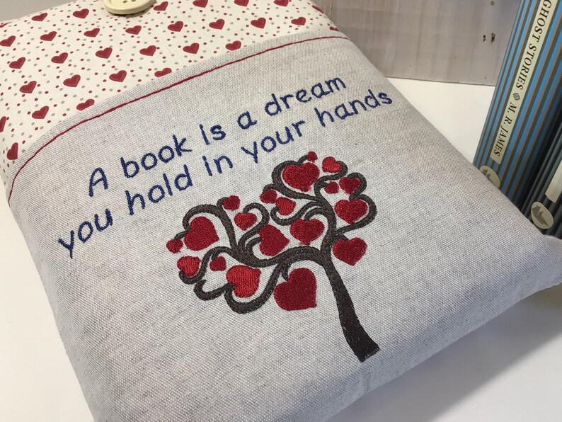 Puede incluir: Una funda de libro gris con corazones rojos y el texto "Un libro es un sue&ntilde;o que tienes en tus manos".