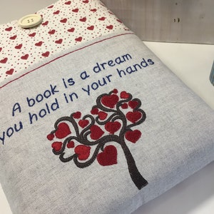 Puede incluir: Una funda de libro gris con un dise&ntilde;o de &aacute;rbol de corazones rojos y el texto "Un libro es un sue&ntilde;o que tienes en tus manos".