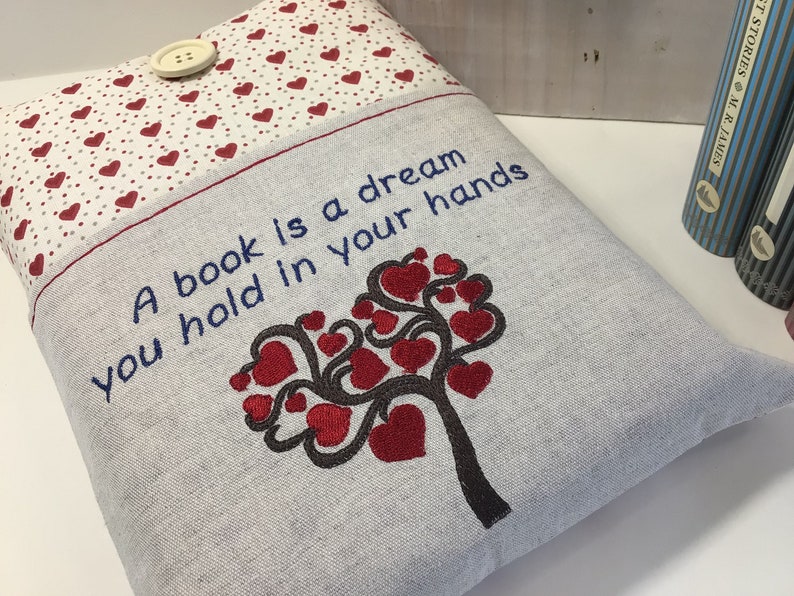 Puede incluir: Una funda de libro gris con un dise&ntilde;o de &aacute;rbol de corazones rojos y el texto "Un libro es un sue&ntilde;o que tienes en tus manos".