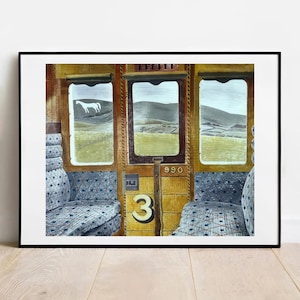 Op de afbeelding: Ingelijst kunstwerk dat het interieur van een treinwagon met drie ramen afbeeldt. De ramen tonen een landschap met glooiende heuvels en een wit paard. Het nummer "3" is zichtbaar op de muur, samen met het nummer "990". De stoelen hebben een blauw-wit patroon.