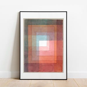 Op de afbeelding: Abstract aquarel schilderij in een zwarte lijst. Het kunstwerk toont een reeks concentrische vierkanten in tinten rood, oranje, bruin en blauw, waardoor een gradiënteffect ontstaat. Het schilderij wordt tentoongesteld aan een witte muur boven een houten vloer.