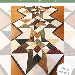 May include: A quilted table runner with a geometric pattern of stars in shades of brown, green, white, and cream. The runner is edged with a dark brown trim. The text "COTTAGE STARS" and "FAT QUARTER & SCRAPPY FRIENDLY!" is printed below the runner. The text "2 Sizes Included!" is printed on a white circle with a brown border.