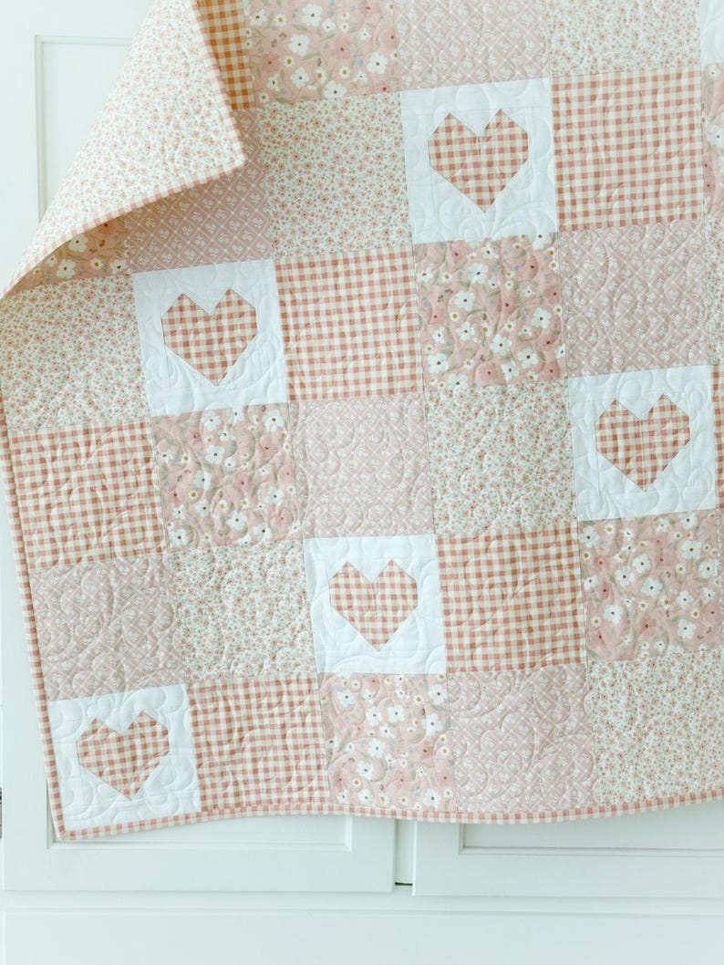 May include: A pink and white patchwork quilt with a heart design. The quilt is made of different fabrics, including gingham and floral prints.