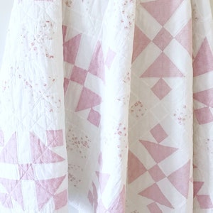 Peut inclure: Une courtepointe rose et blanche avec un motif g&eacute;om&eacute;trique. La courtepointe est en tissu de coton et a une texture douce et matelass&eacute;e.