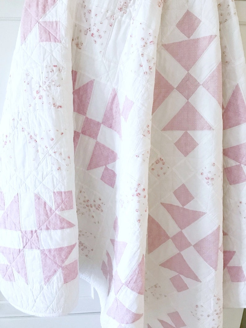 Peut inclure: Une courtepointe rose et blanche avec un motif g&eacute;om&eacute;trique. La courtepointe est en tissu de coton et a une texture douce et matelass&eacute;e.