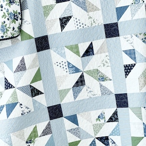 May include: A white quilt with a blue, green, and white geometric pattern. The quilt is made of various fabrics with different patterns, including stripes, floral prints, and polka dots.