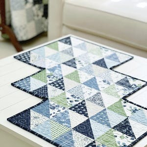 K&ouml;nnte beinhalten: Ein blauer und gr&uuml;ner Patchwork-Tischl&auml;ufer mit einem geometrischen Muster aus Dreiecken. Der L&auml;ufer besteht aus verschiedenen Stoffen mit floralen und geometrischen Drucken.
