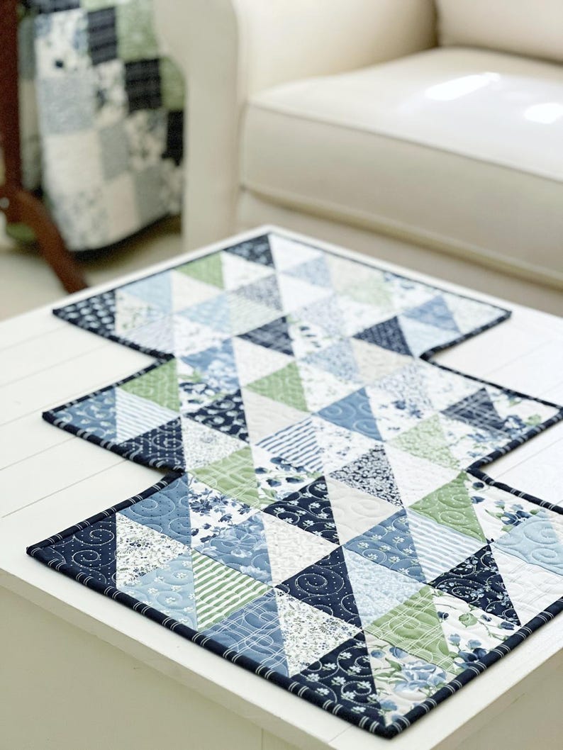 K&ouml;nnte beinhalten: Ein blauer und gr&uuml;ner Patchwork-Tischl&auml;ufer mit einem geometrischen Muster aus Dreiecken. Der L&auml;ufer besteht aus verschiedenen Stoffen mit floralen und geometrischen Drucken.