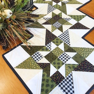 May include: A white table runner with a black and white checkered pattern and green floral fabric. The runner is trimmed with a black and white polka dot trim.