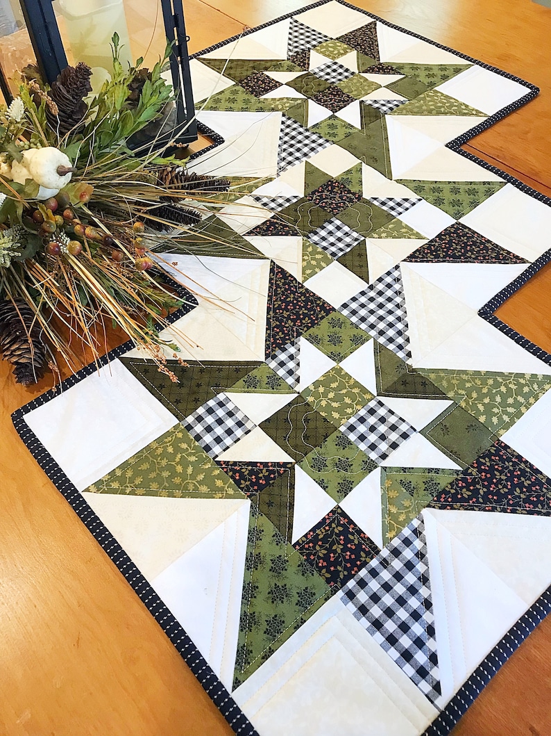 May include: A white table runner with a black and white checkered pattern and green floral fabric. The runner is trimmed with a black and white polka dot trim.