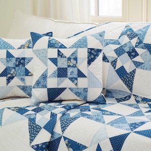 Peut inclure: Une courtepointe blanche et bleue en patchwork avec un motif d'&eacute;toile. La courtepointe est faite de diff&eacute;rents tons de tissu bleu et a un fond blanc. La courtepointe est pli&eacute;e et expos&eacute;e sur un lit avec deux housses de coussin assorties.