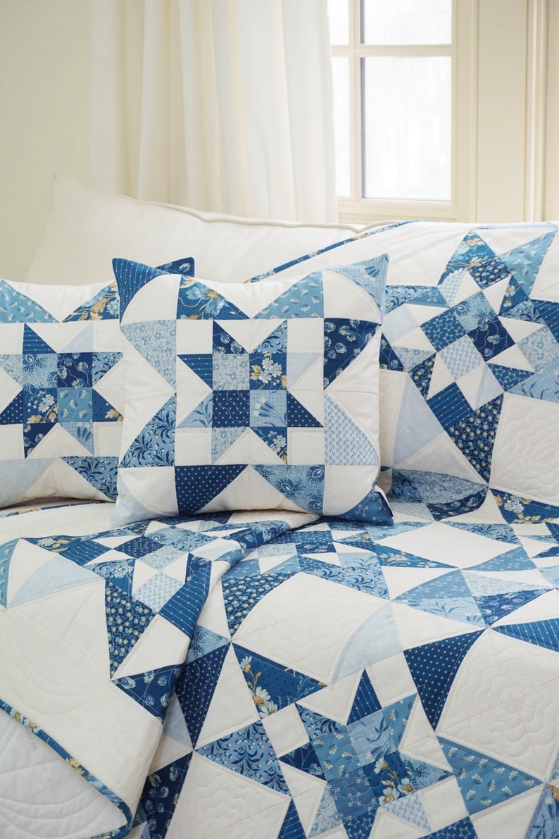 Peut inclure: Une courtepointe blanche et bleue en patchwork avec un motif d'&eacute;toile. La courtepointe est faite de diff&eacute;rents tons de tissu bleu et a un fond blanc. La courtepointe est pli&eacute;e et expos&eacute;e sur un lit avec deux housses de coussin assorties.