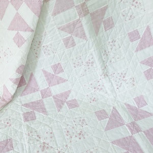 Peut inclure: Une courtepointe blanche avec un motif rose et blanc. La courtepointe est faite de carr&eacute;s et de triangles, et le tissu rose a un petit imprim&eacute; floral.