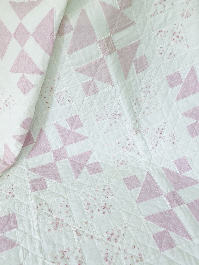 Peut inclure: Une courtepointe blanche avec un motif rose et blanc. La courtepointe est faite de carr&eacute;s et de triangles, et le tissu rose a un petit imprim&eacute; floral.
