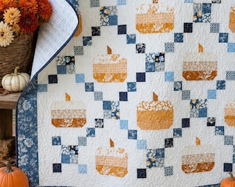 May include: A quilt featuring a repeating pattern of orange and white pumpkin shapes arranged in a grid. The design incorporates blue and white floral and geometric fabric squares, with a dark blue floral border and white quilted background.