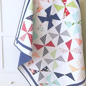May include: A white quilt with a navy blue border and a pattern of colourful pinwheels. The quilt is made of various fabrics with floral and geometric designs.