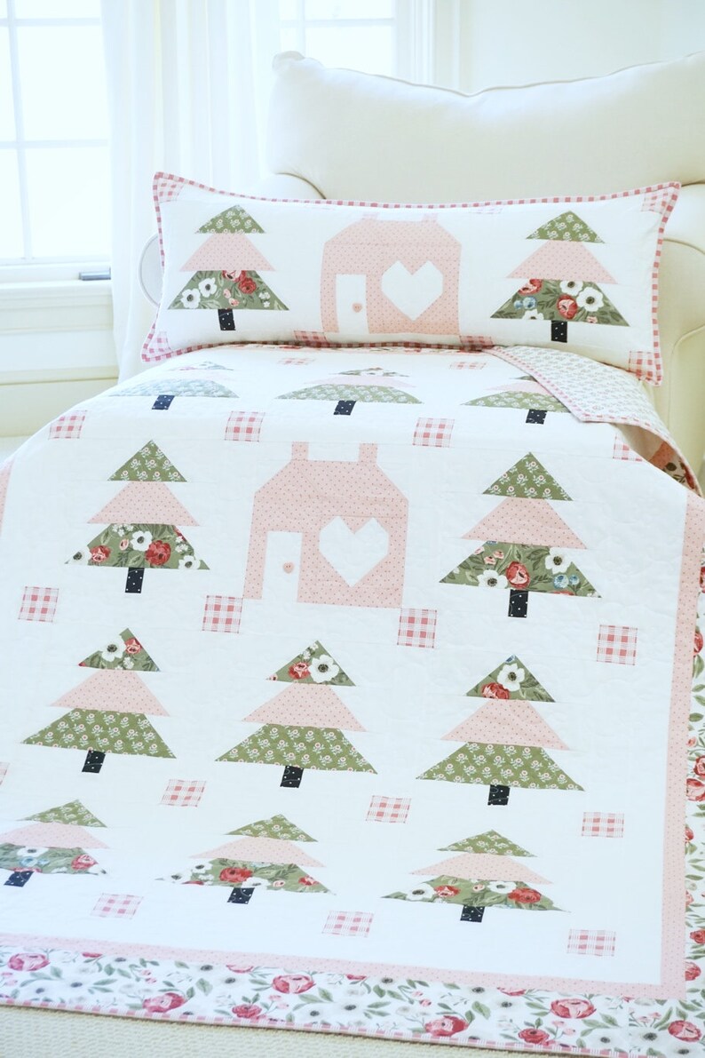 Puede incluir: Una colcha blanca con un patr&oacute;n floral rosa y verde. La colcha presenta una casa con un coraz&oacute;n recortado y varios &aacute;rboles. La colcha est&aacute; hecha con una variedad de telas y es perfecta para una guarder&iacute;a o habitaci&oacute;n de un ni&ntilde;o.