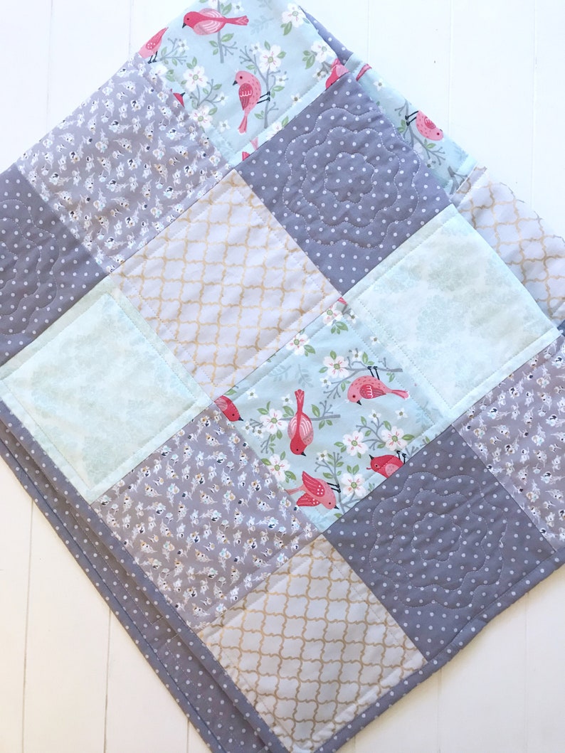 May include: A patchwork quilt with a gray, white, and blue color scheme. The quilt is made of different fabrics with floral and geometric patterns. The quilt is quilted with a decorative stitch.