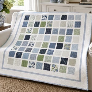 May include: A patchwork quilt featuring a grid of square fabric blocks in various shades of blue, navy, and sage green. The blocks display diverse patterns including floral prints, stripes, and solid textures, all bordered by a white frame.