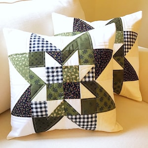 May include: Two decorative throw pillows with a starburst pattern in shades of green, black, and white. The pillows are made of fabric with a patchwork design.