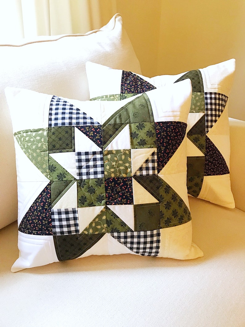 May include: Two decorative throw pillows with a starburst pattern in shades of green, black, and white. The pillows are made of fabric with a patchwork design.