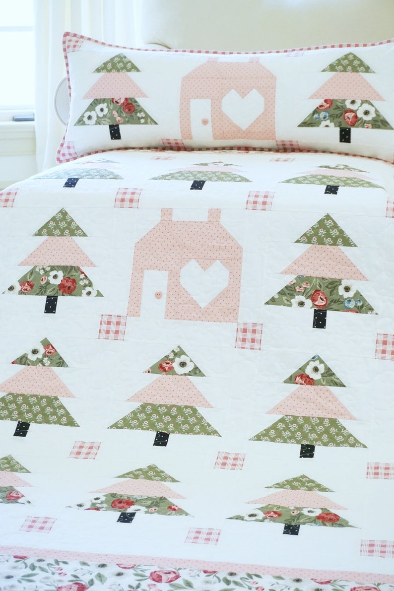 Puede incluir: Una colcha blanca con un dise&ntilde;o de patchwork rosa y verde. La colcha presenta una casa con un coraz&oacute;n recortado y varios &aacute;rboles. Los &aacute;rboles est&aacute;n hechos de tela rosa, verde y blanca con patrones florales.