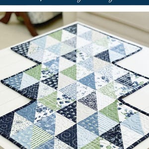 K&ouml;nnte beinhalten: Ein blauer und gr&uuml;ner Patchwork-Tischl&auml;ufer mit einem geometrischen Muster aus Dreiecken. Der L&auml;ufer hei&szlig;t "Charming Waves" und umfasst zwei Gr&ouml;&szlig;en.