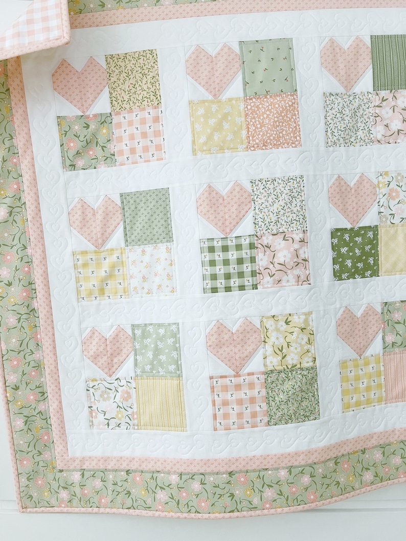 K&ouml;nnte beinhalten: Eine rosafarbene und gr&uuml;ne Patchwork-Decke mit einem Herz-Design. Die Decke besteht aus verschiedenen floralen und karierten Stoffen.