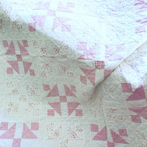 Peut inclure: Une courtepointe blanche avec un motif floral rose et blanc. La courtepointe est pli&eacute;e en deux et le motif floral rose et blanc est visible des deux c&ocirc;t&eacute;s.