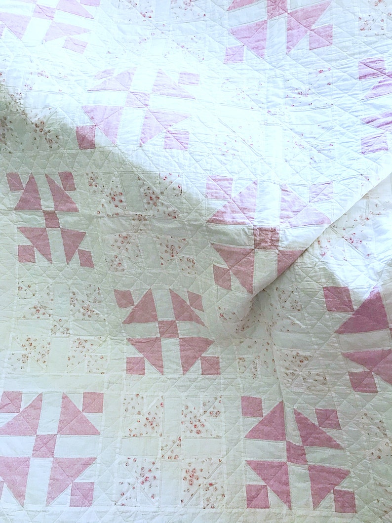 Peut inclure: Une courtepointe blanche avec un motif floral rose et blanc. La courtepointe est pli&eacute;e en deux et le motif floral rose et blanc est visible des deux c&ocirc;t&eacute;s.