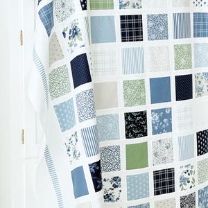 May include: A white quilt with a patchwork design featuring squares of various blue, green, and white patterned fabrics.