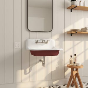 May include: A wall-mounted bathroom sink with a white basin and a deep red-colored bowl. The sink has chrome fixtures and is set against a white paneled wall. A mirror hangs above the sink, and a small wooden stool sits nearby.
