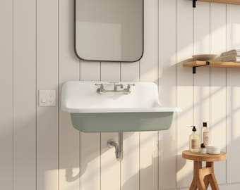 May include: A white and sage green wall-mounted sink with chrome fixtures. The sink is set against a white paneled wall, with a black-framed mirror above. A small wooden stool and shelves with toiletries are also visible.