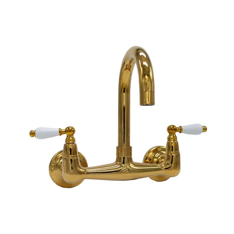 May include: A gold wall-mounted kitchen faucet with white ceramic handles. The faucet has a high arc spout and a traditional design.