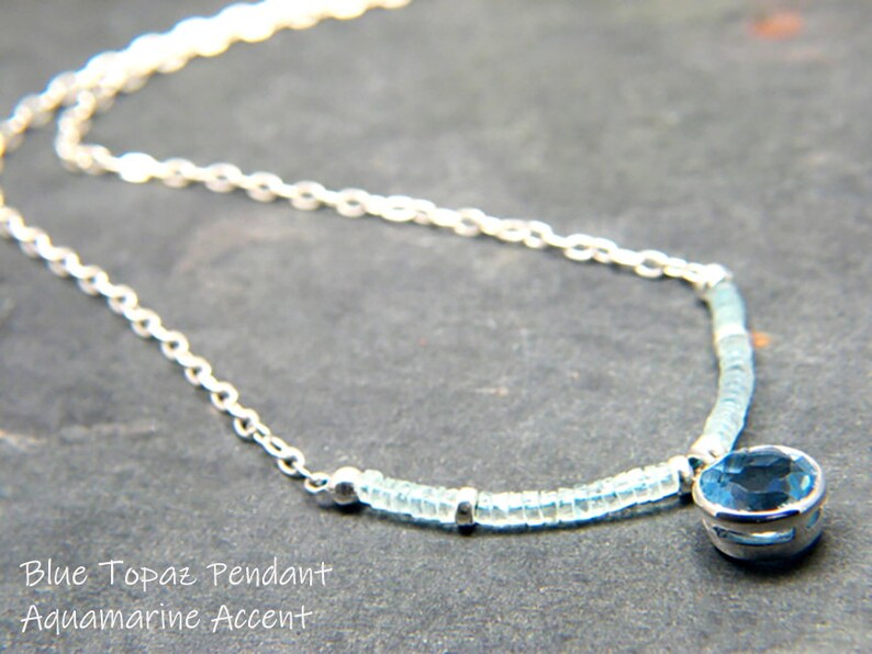 May include: A silver chain necklace with a blue topaz pendant and aquamarine beads. The pendant is a round, faceted stone set in a silver bezel.