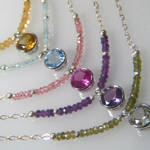 May include: Five silver necklaces with different coloured gemstones. The necklaces feature a variety of beads, including clear, light blue, pink, purple, and green.