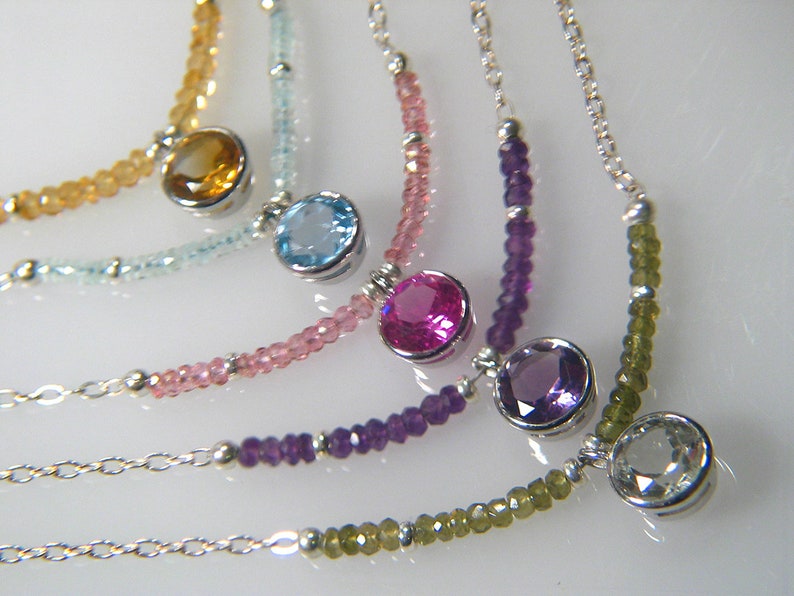 May include: Five silver necklaces with different coloured gemstones. The necklaces feature a variety of beads, including clear, light blue, pink, purple, and green.