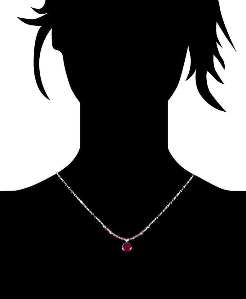 May include: A silver chain necklace with a small, round, red gemstone pendant.