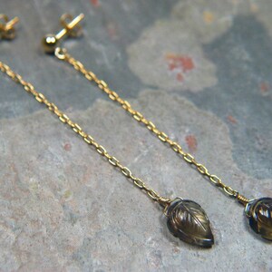 May include: A pair of gold dangle earrings with brown leaf-shaped gemstone pendants.
