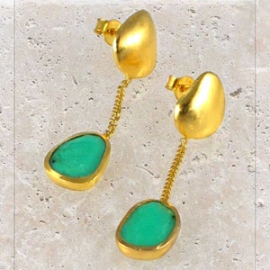 Può includere: Orecchini pendenti in oro con una pietra preziosa verde. Gli orecchini presentano una pietra preziosa a forma di lacrima che pende da una catena d'oro.