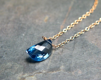 May include: A delicate gold chain necklace with a teardrop-shaped blue gemstone pendant.