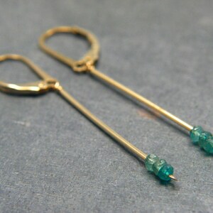 May include: A pair of gold earrings with a long, thin, gold bar and a cluster of teal green gemstones at the end of each bar.