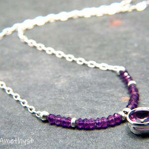May include: A silver chain necklace with a small purple amethyst gemstone pendant. The pendant is surrounded by smaller purple amethyst beads.