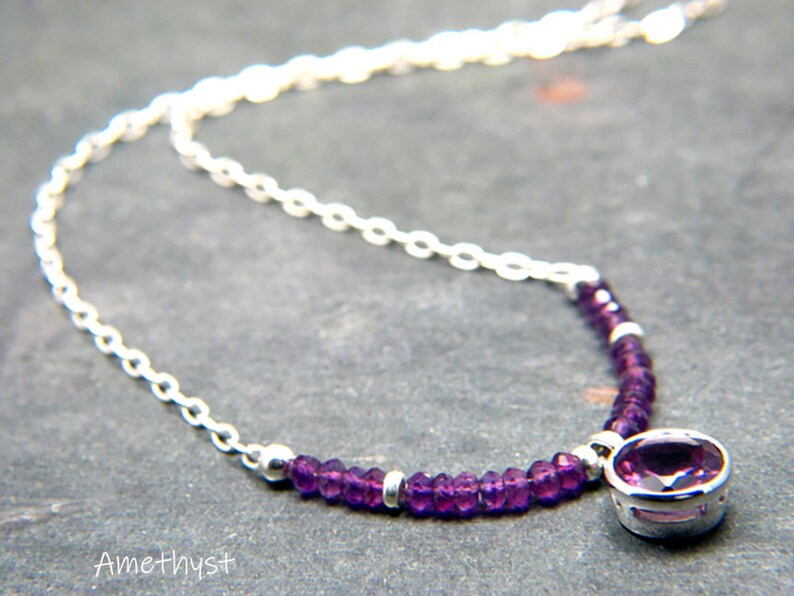 May include: A silver chain necklace with a small purple amethyst gemstone pendant. The pendant is surrounded by smaller purple amethyst beads.