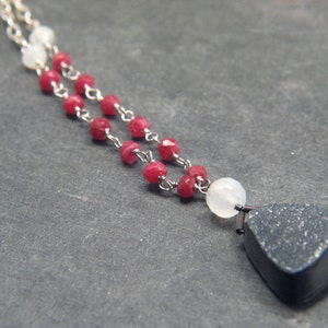 May include: A silver chain necklace with red and white beads and a dark gray stone pendant.