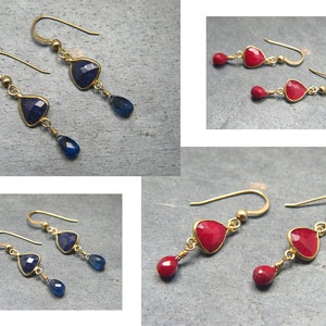May include: A pair of gold earrings with blue gemstone drops. The earrings feature a triangular shaped gemstone with a gold setting.