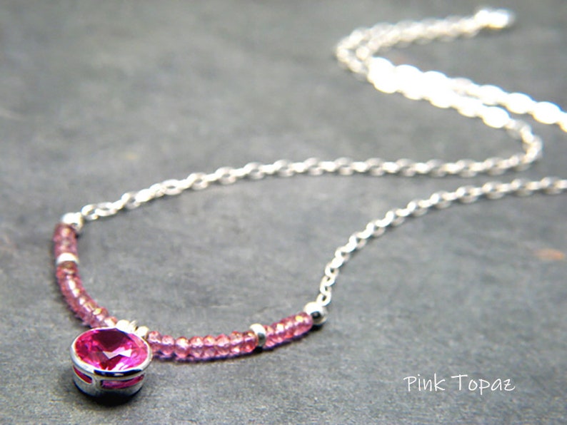 May include: A silver chain necklace with a pink topaz gemstone pendant and pink topaz beads. The pendant is set in a silver bezel.