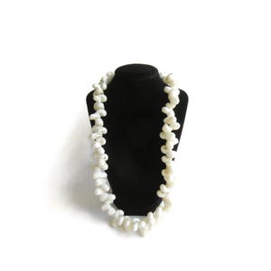 May include: A white beaded necklace made of irregular shaped beads. The necklace is displayed on a black velvet bust form.