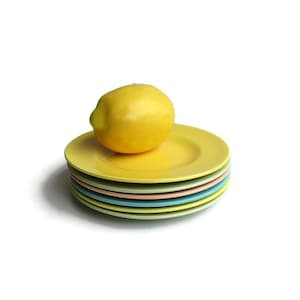 May include: A stack of six pastel-colored ceramic plates with a yellow lemon on top. The plates are in shades of yellow, green, blue, and pink.