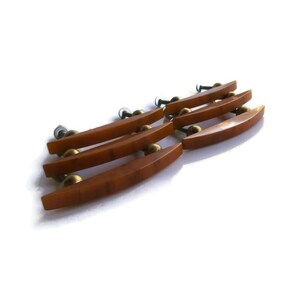 May include: A set of three amber-colored, curved drawer pulls with a smooth finish. Each handle features two brass-toned metal mounting posts with screws attached to the back, designed for horizontal installation on furniture cabinetry.